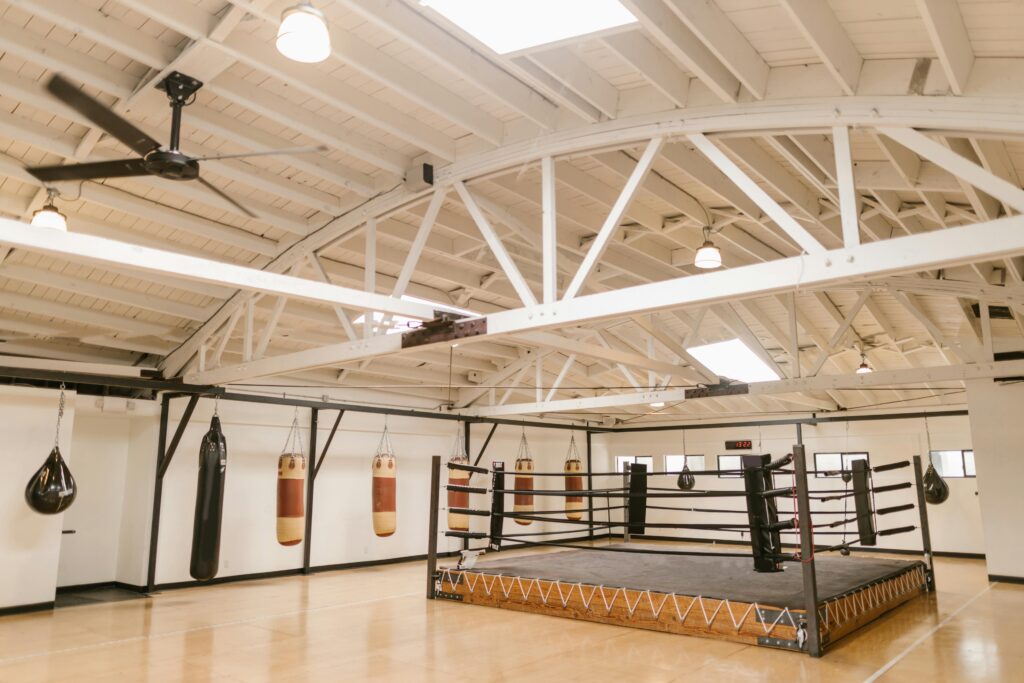 A clean and empty boxing gym with punching bags and a ring, ready for training.